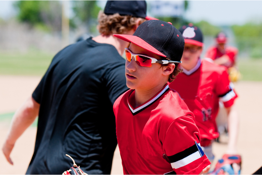 A boy wearing a red baseball uniform and stylish sunglasses