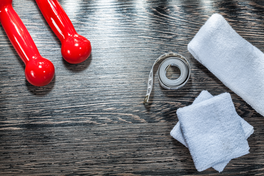 White basketball headband and sweatbands, measuring tape, and red dumbbells on a wood table