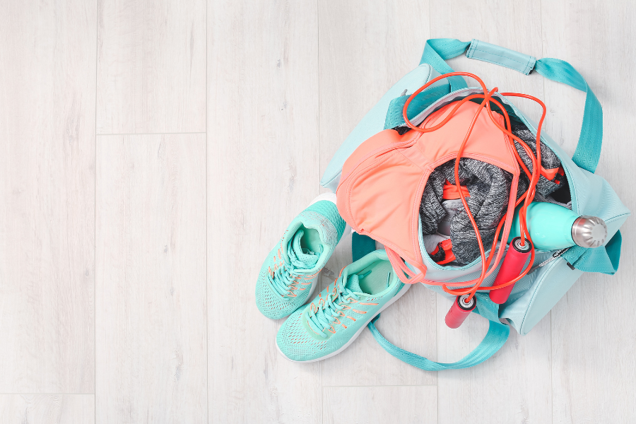A gym bag full of workout supplies next to a pair or fitness shoes